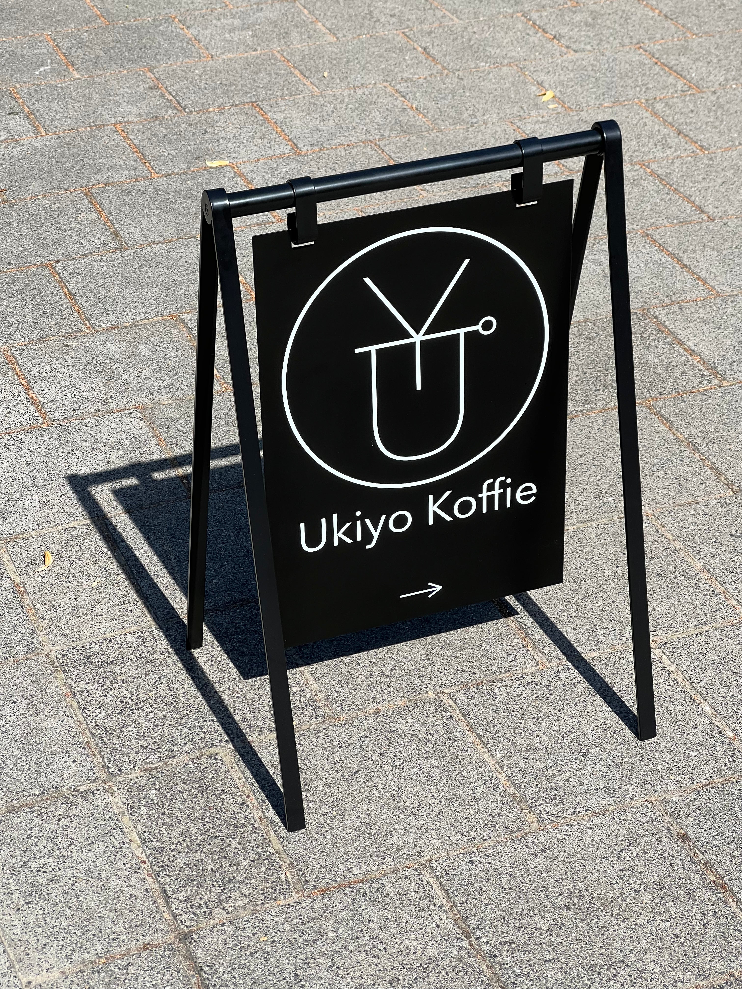 A black metal A-frame sidewalk sign with white text reading 'Ukiyo Koffie'